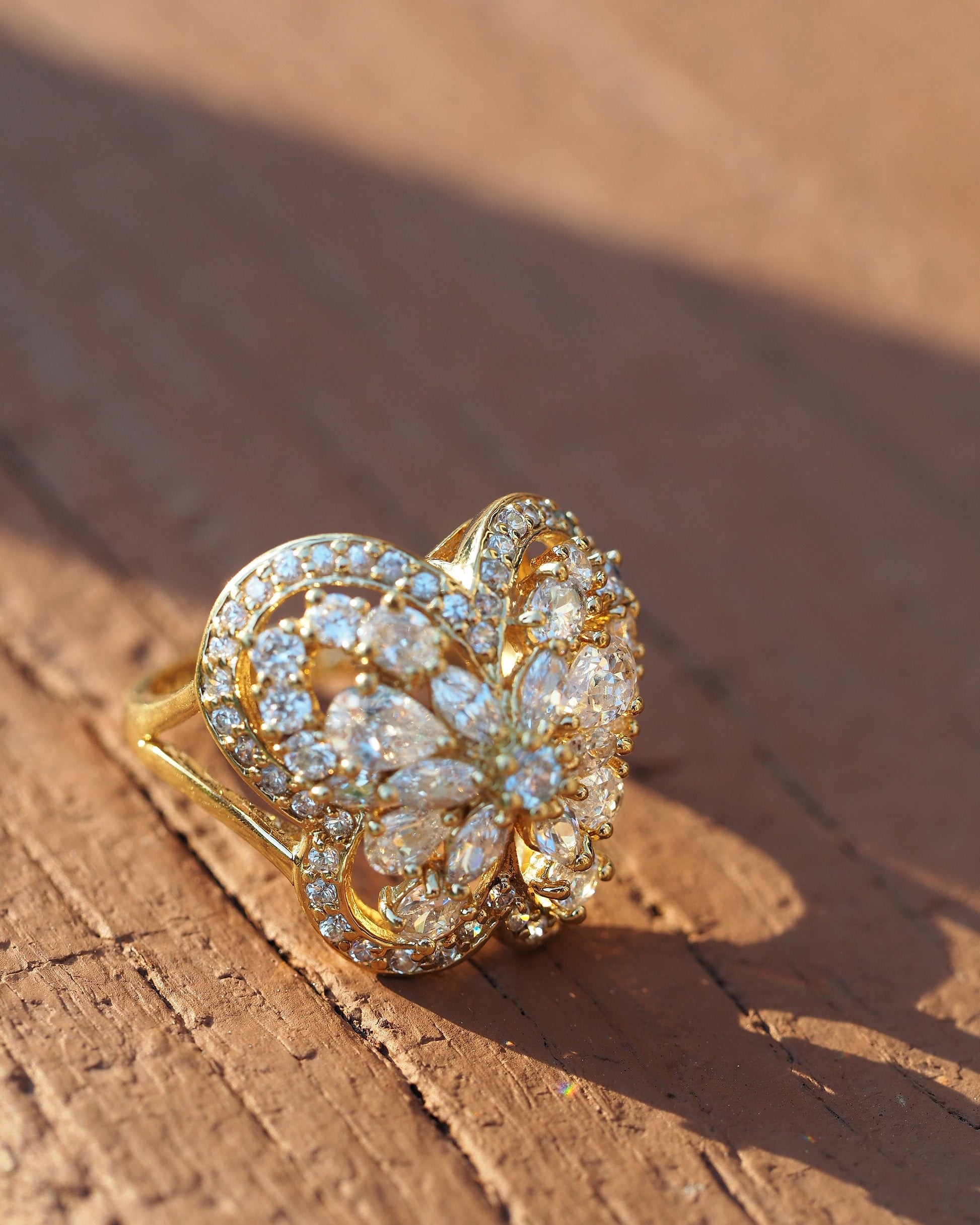 Gold vermeil butterfly ring with rhinestone-set wings in openwork design, front three-quarter view on wood surface