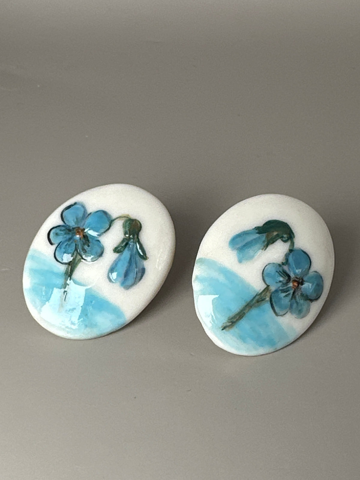 Top view of ceramic earrings showing hand-painted floral motifs with blue flowers and pale blue horizon bands