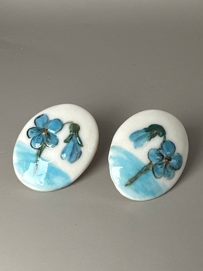 Top view of ceramic earrings showing hand-painted floral motifs with blue flowers and pale blue horizon bands