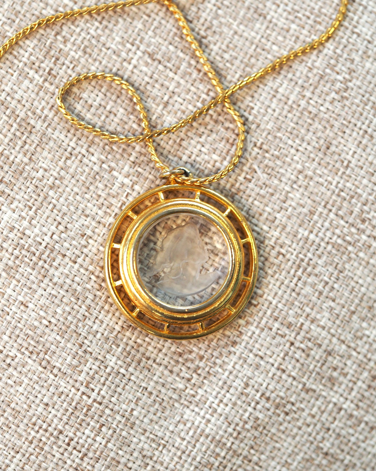 Back view of gold-tone openwork pendant frame with carved glass cameo center on twisted rope chain