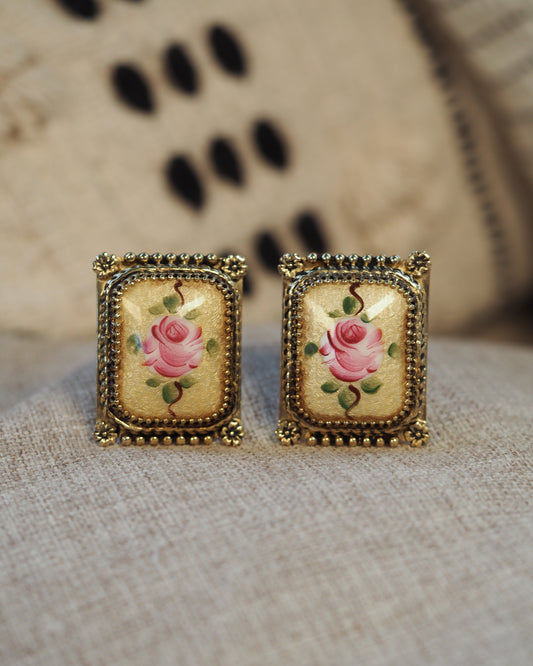 Pair of gold-tone rectangular clip-on earrings with hand-painted pink rose porcelain insets, front view on neutral surface