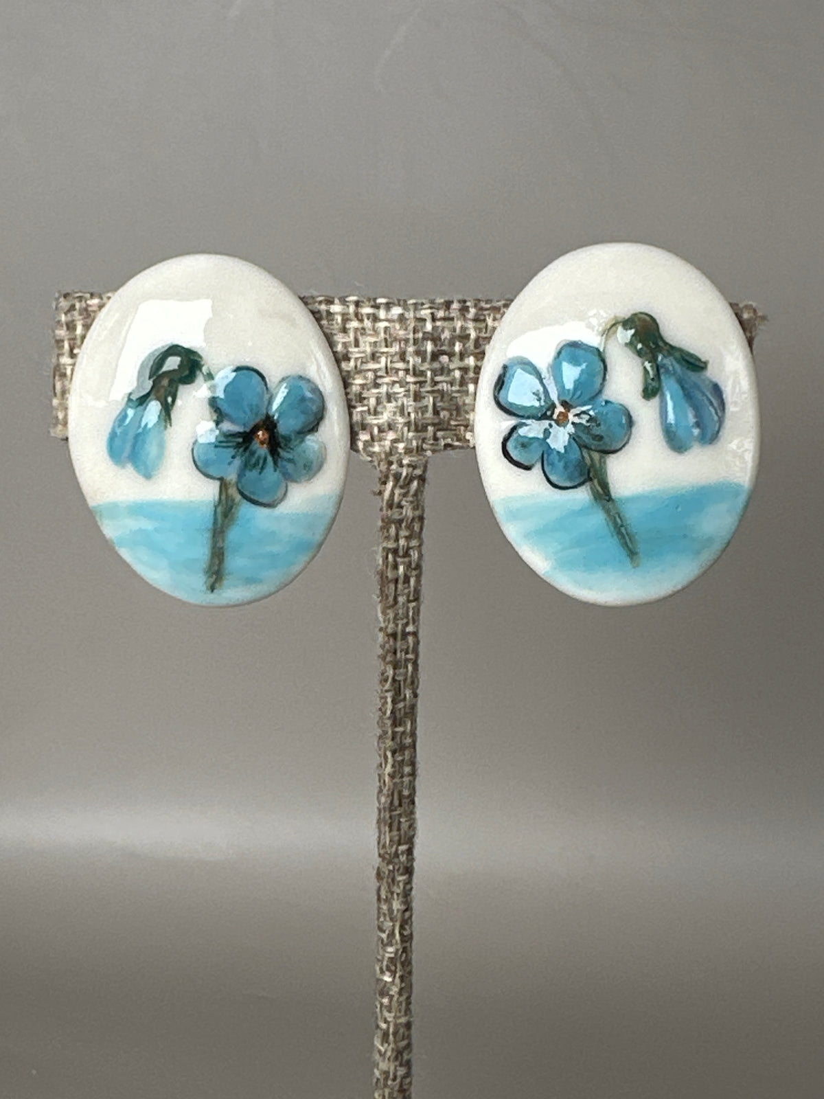 Mid-Century hand-painted ceramic screwback earrings with blue floral decoration, front view on display stand