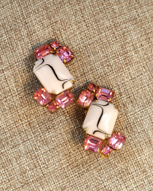 Pair of mid-century clip earrings with white glass cabochon centers and pink rhinestones in gold-tone metal, front view on linen