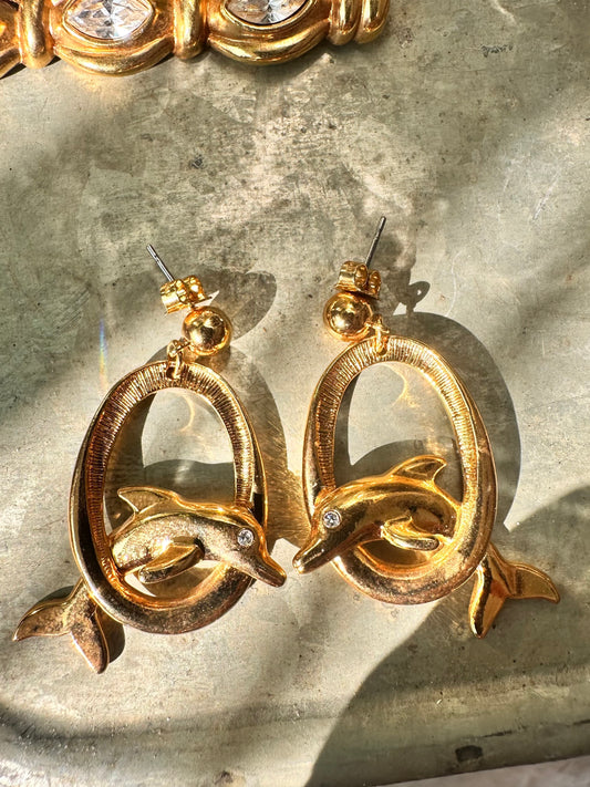 Pair of vintage Avon gold-tone dolphin dangle earrings with textured oval hoops and rhinestone eyes, front view on white background
