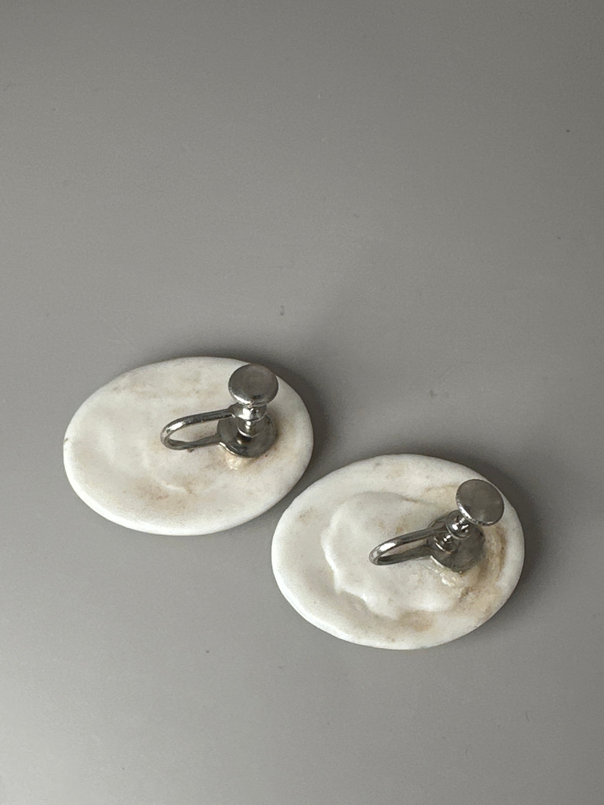 Reverse side of ceramic earrings showing screw-back closures with flat discs and threaded posts