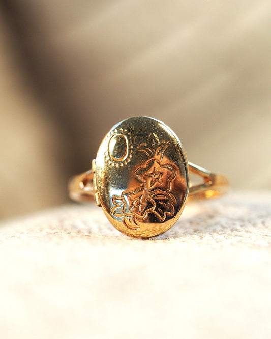 Vintage 8K gold electroplate locket ring with engraved floral motif on oval face, front view on textured surface