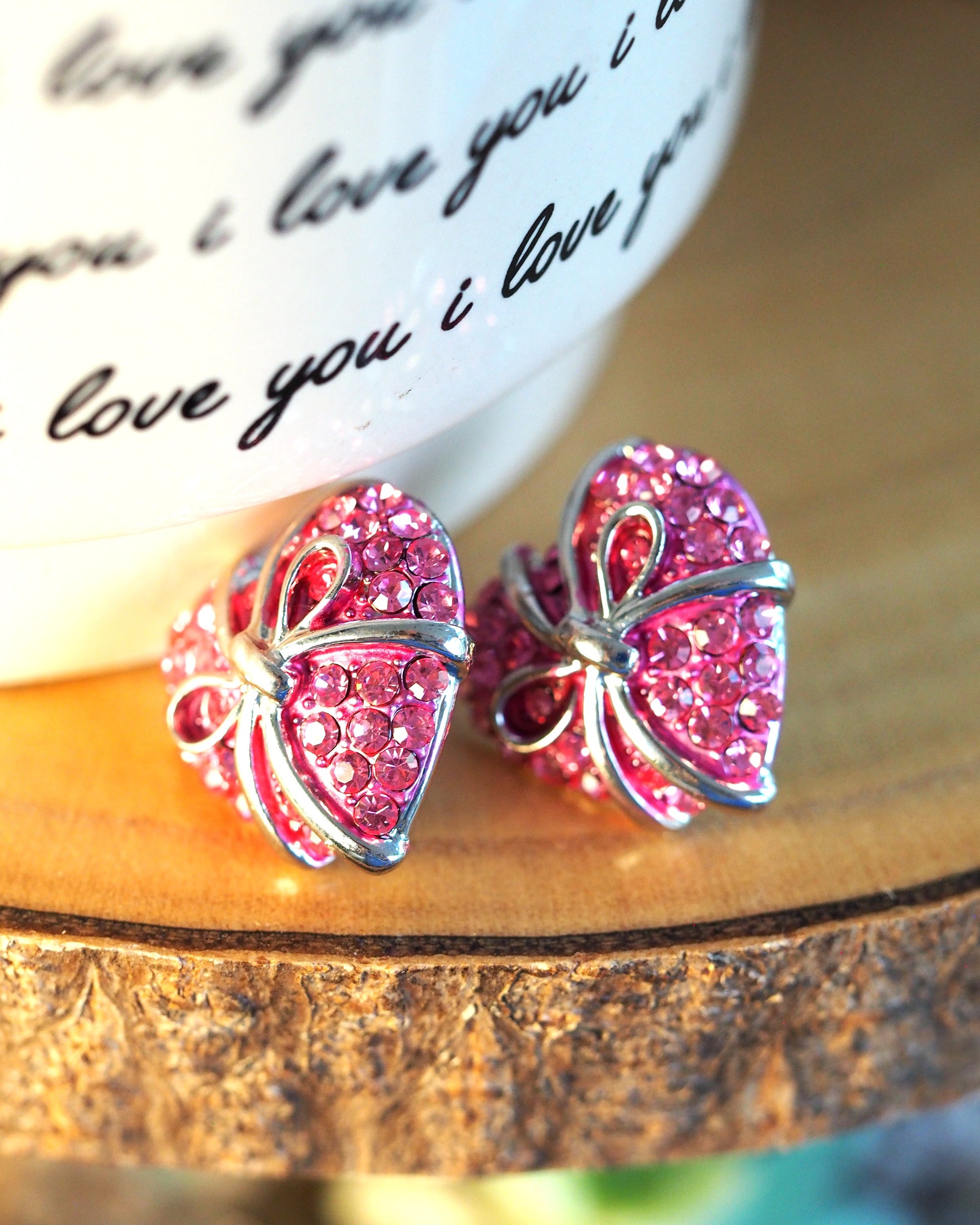 1980s pink rhinestone heart earrings with silver-tone bows, angled side view on wood stand