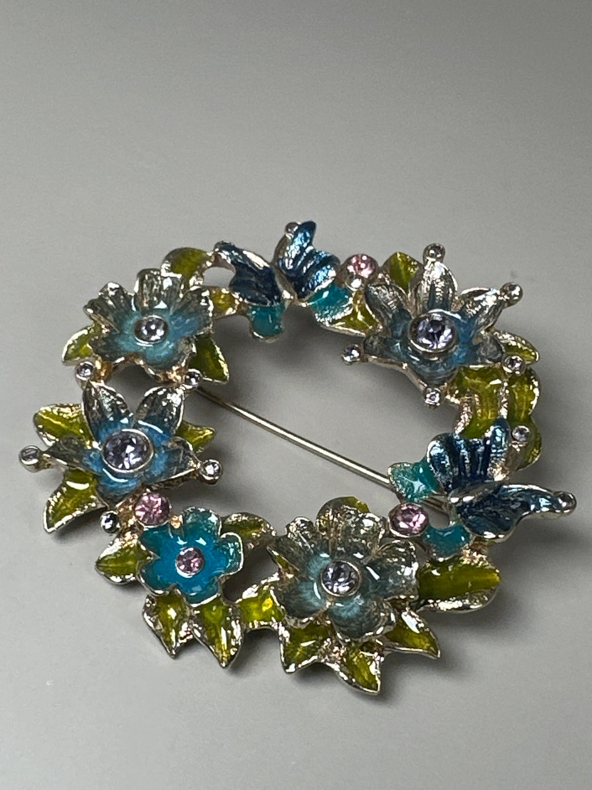 Front view of Napier enamel floral wreath brooch flat on surface, showing teal, pink, lavender, and chartreuse flowers with butterflies