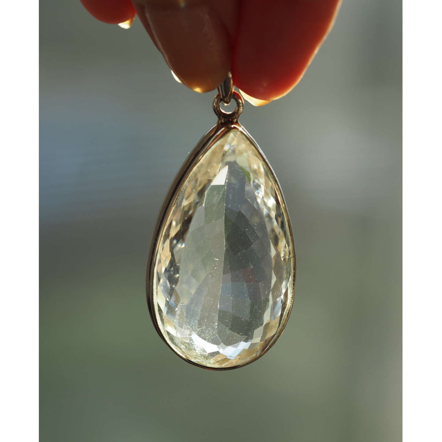 Faceted clear teardrop pendant held to natural light