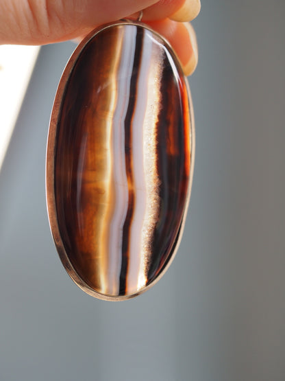 Close-up of large banded agate pendant showing the polished striped stone and natural druzy-crystal seam