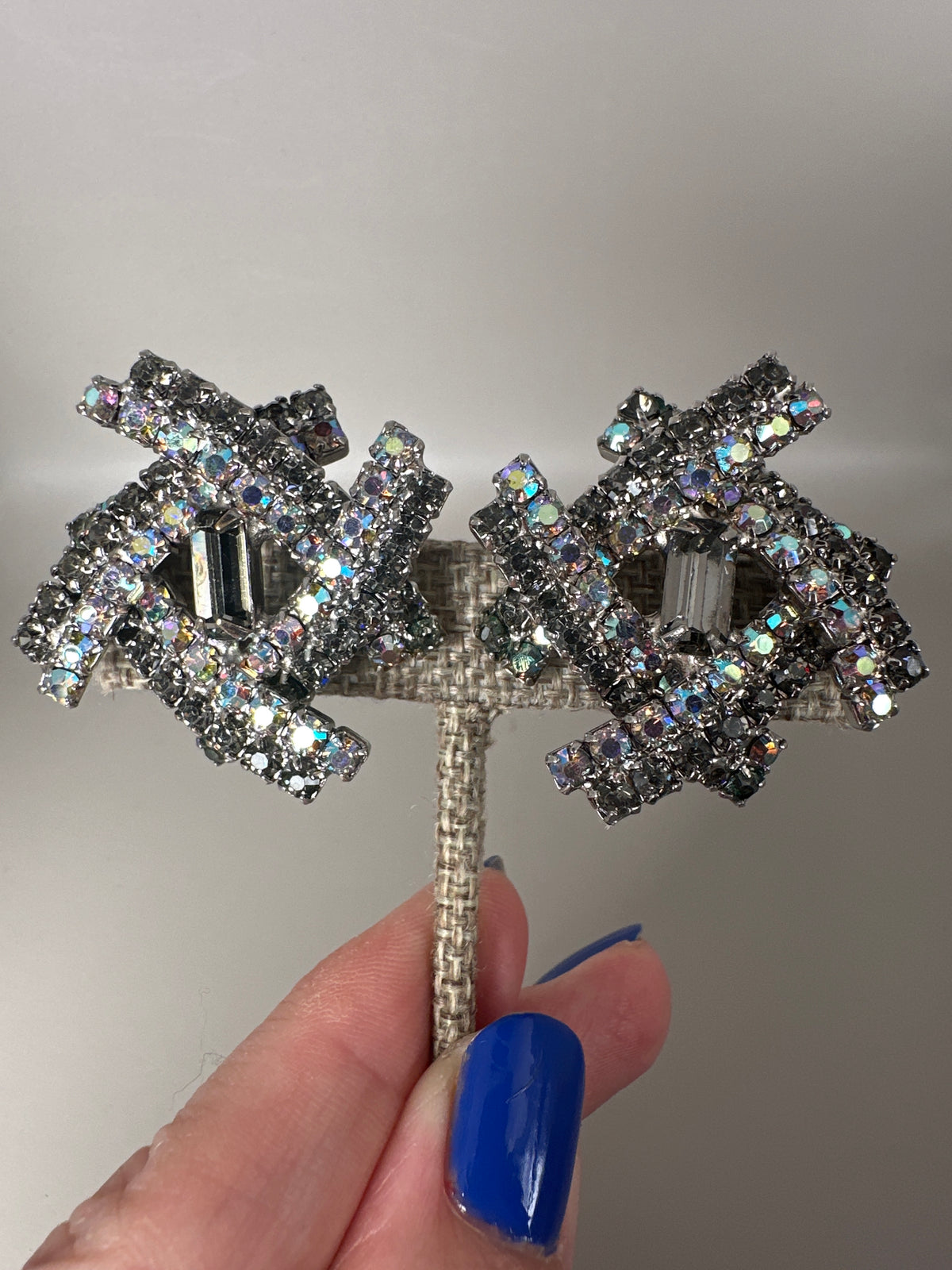 Clip earrings held on fingertips for scale, showing AB rhinestone sparkle and dimensional construction