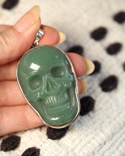 Aventurine skull pendant held in hand for scale, showing 2.25-inch drop and oversized presence below collarbone