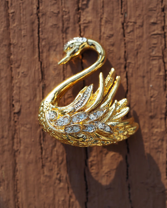 Marvella gold-tone swan brooch with rhinestone-set wings, front view on wood surface