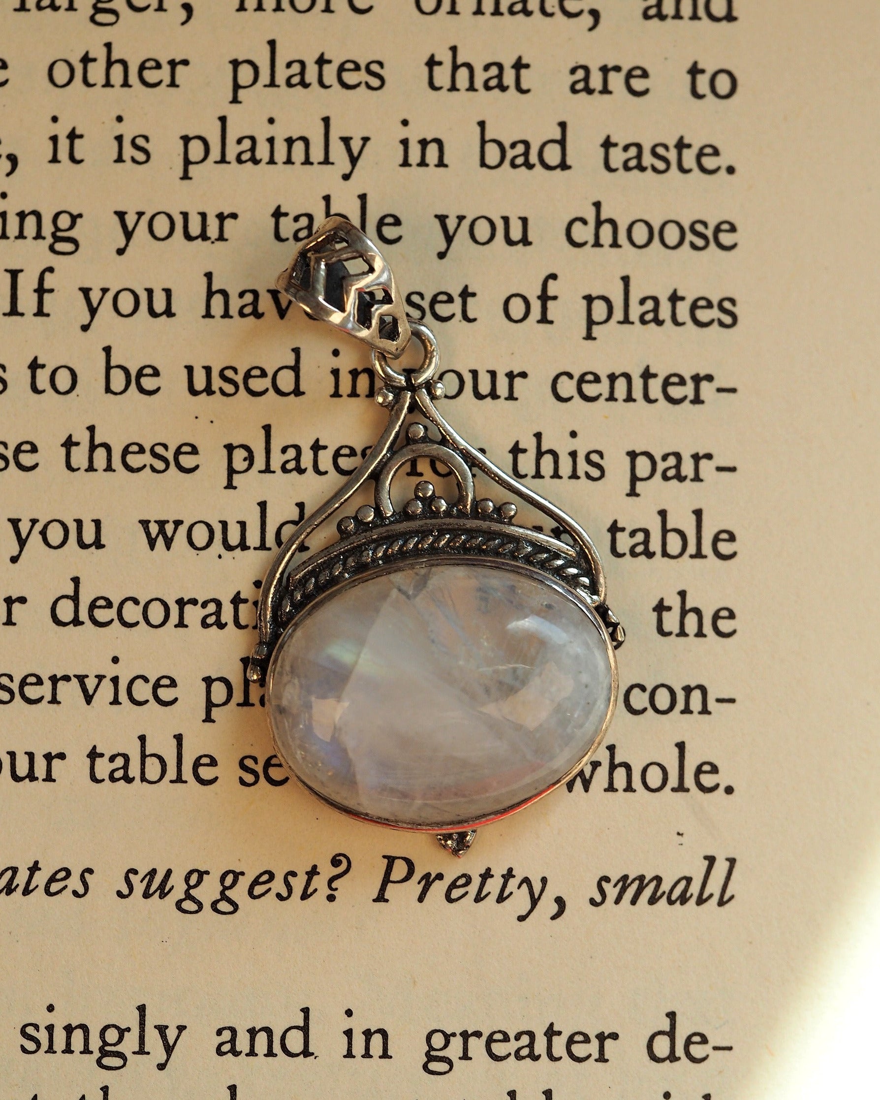 Sterling silver moonstone pendant with filigree bail, overhead view showing faceted stone and scrollwork detail