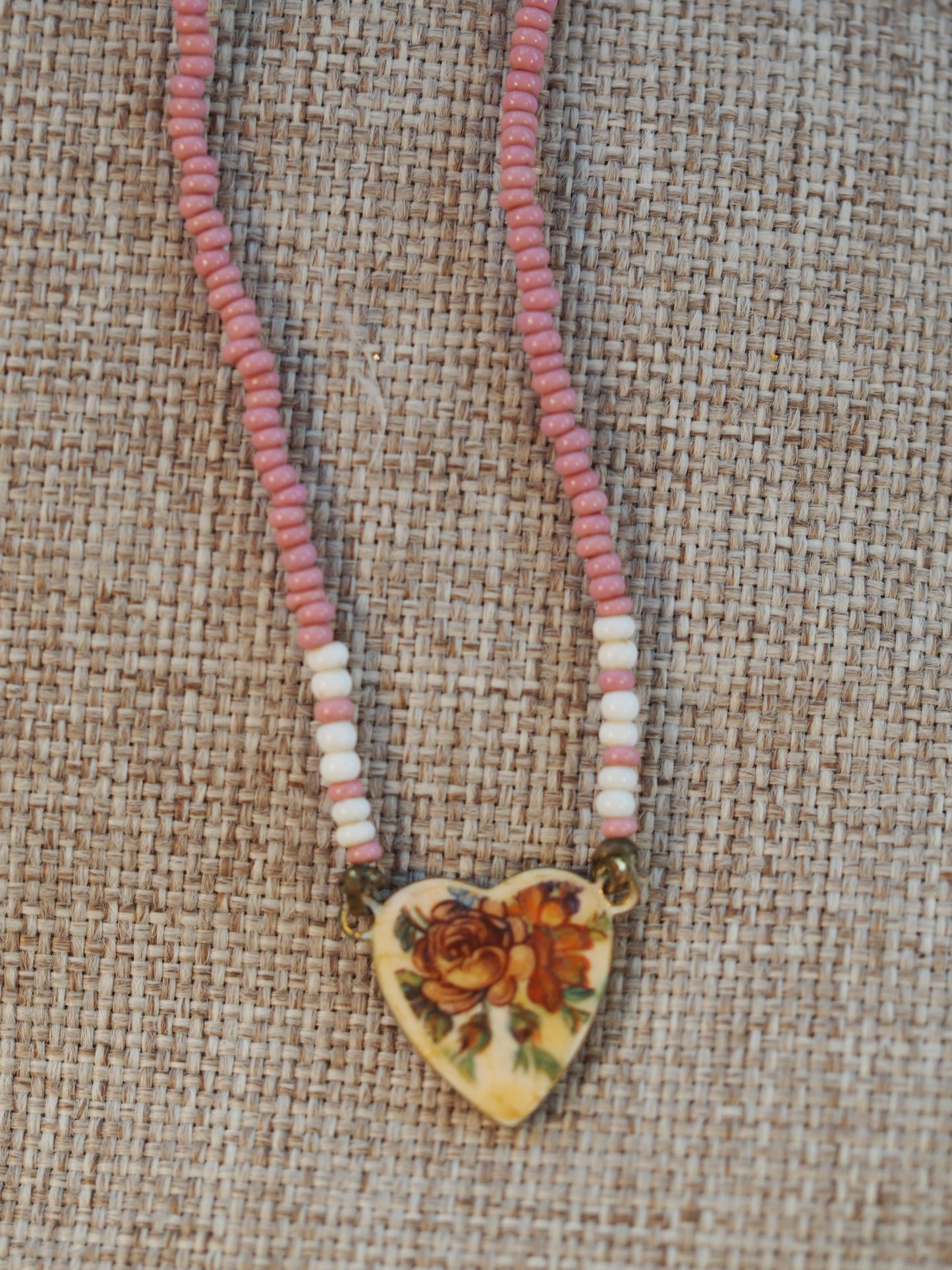 Pink and white seed bead necklace with brass heart charm featuring an orange rose transfer, front view