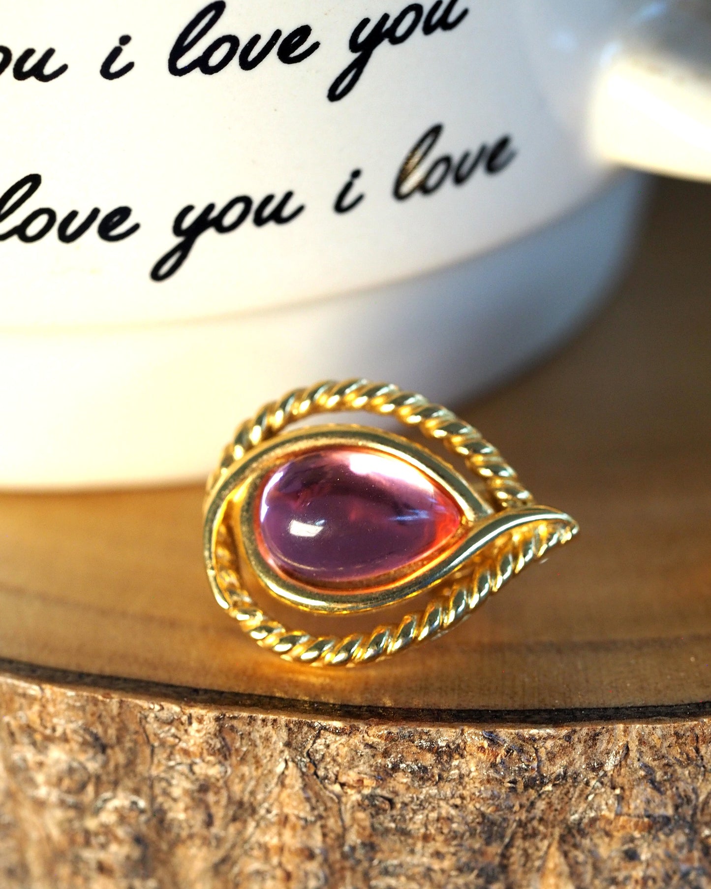 Close-up of a translucent pink teardrop cabochon in a double gold-tone rope-twist frame
