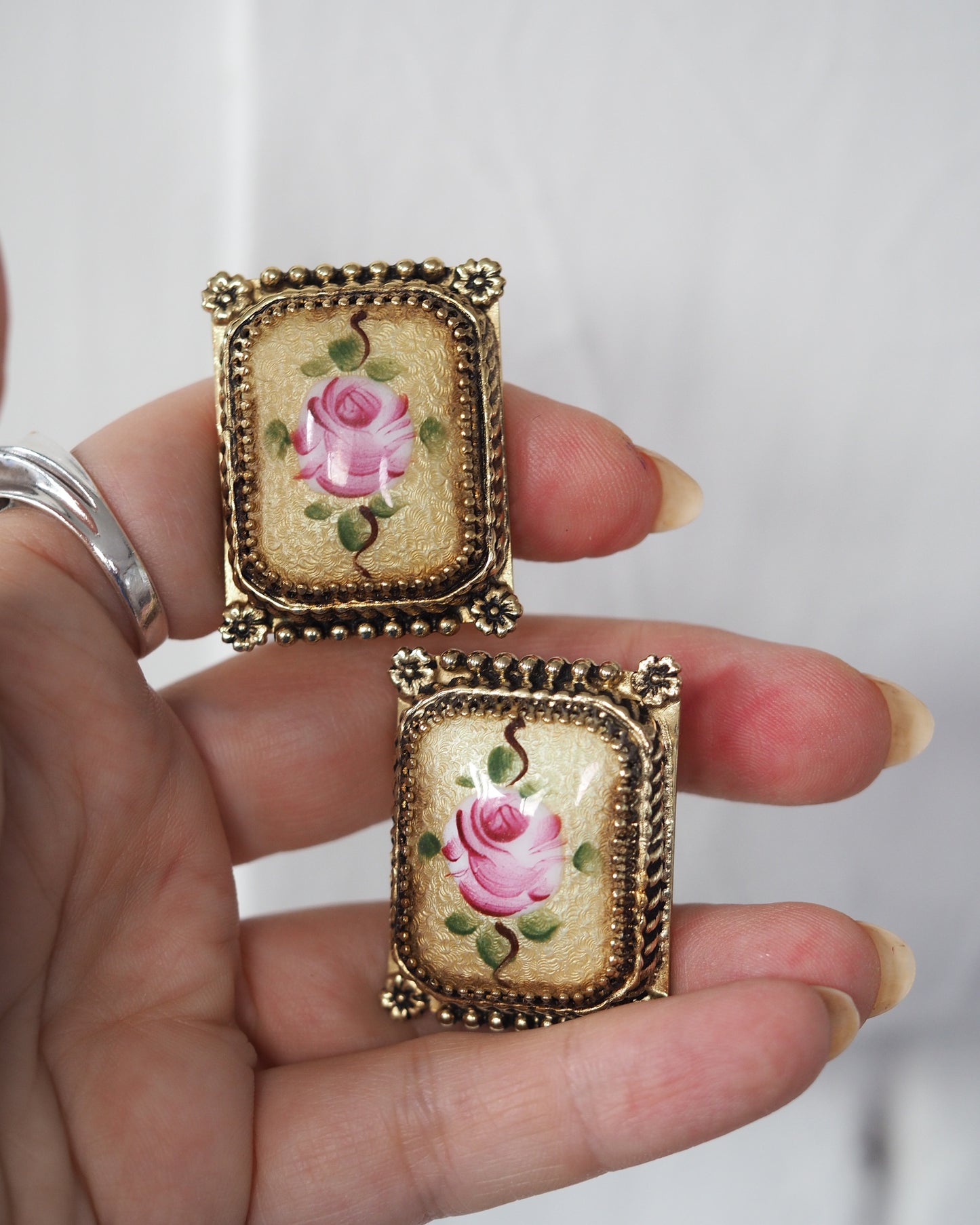 Pair of earrings held in hand for scale, showing size against fingertips