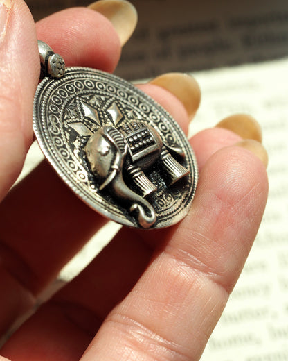 Sterling silver elephant pendant with high-relief detail and beaded borders, front view held on fingertips