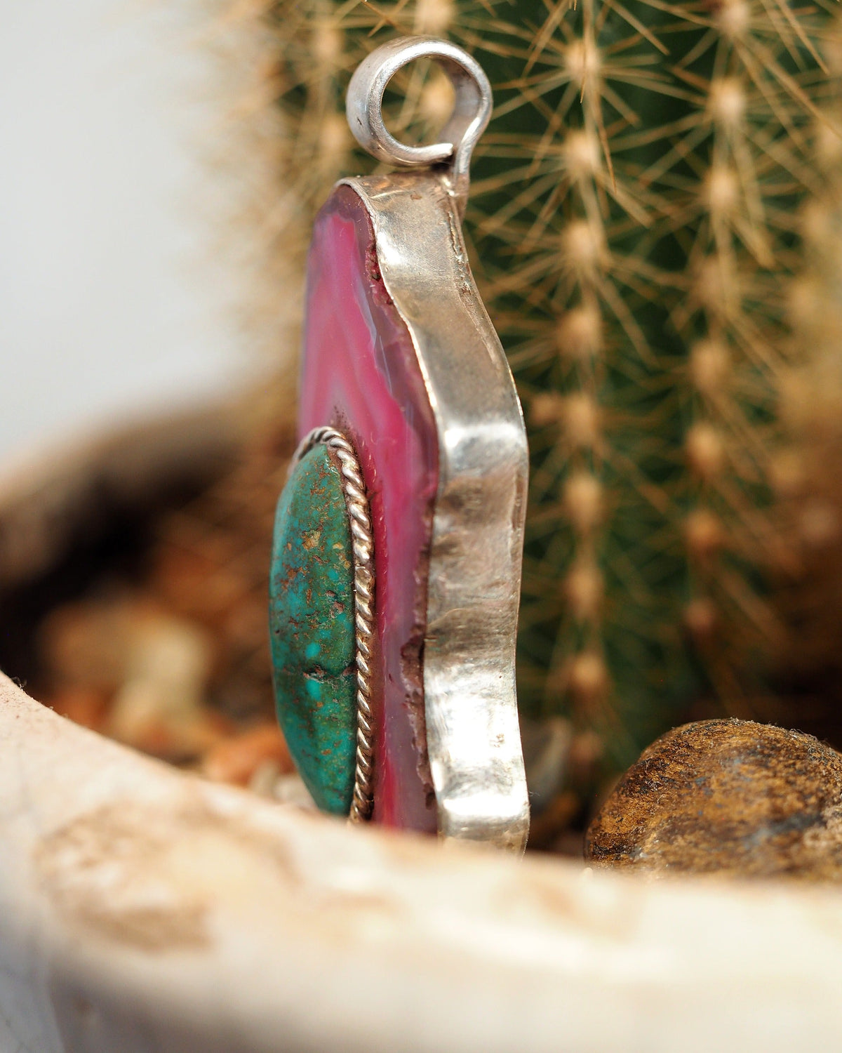 Side view of dyed pink agate pendant showing raised cabochon bezel and silver-tone edge setting