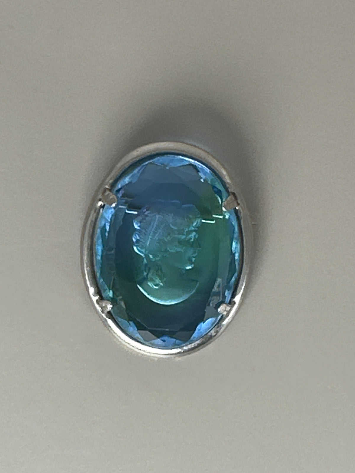 Blue glass cameo brooch, front view on flat surface, showing engraved geometric border on silver-tone metal frame