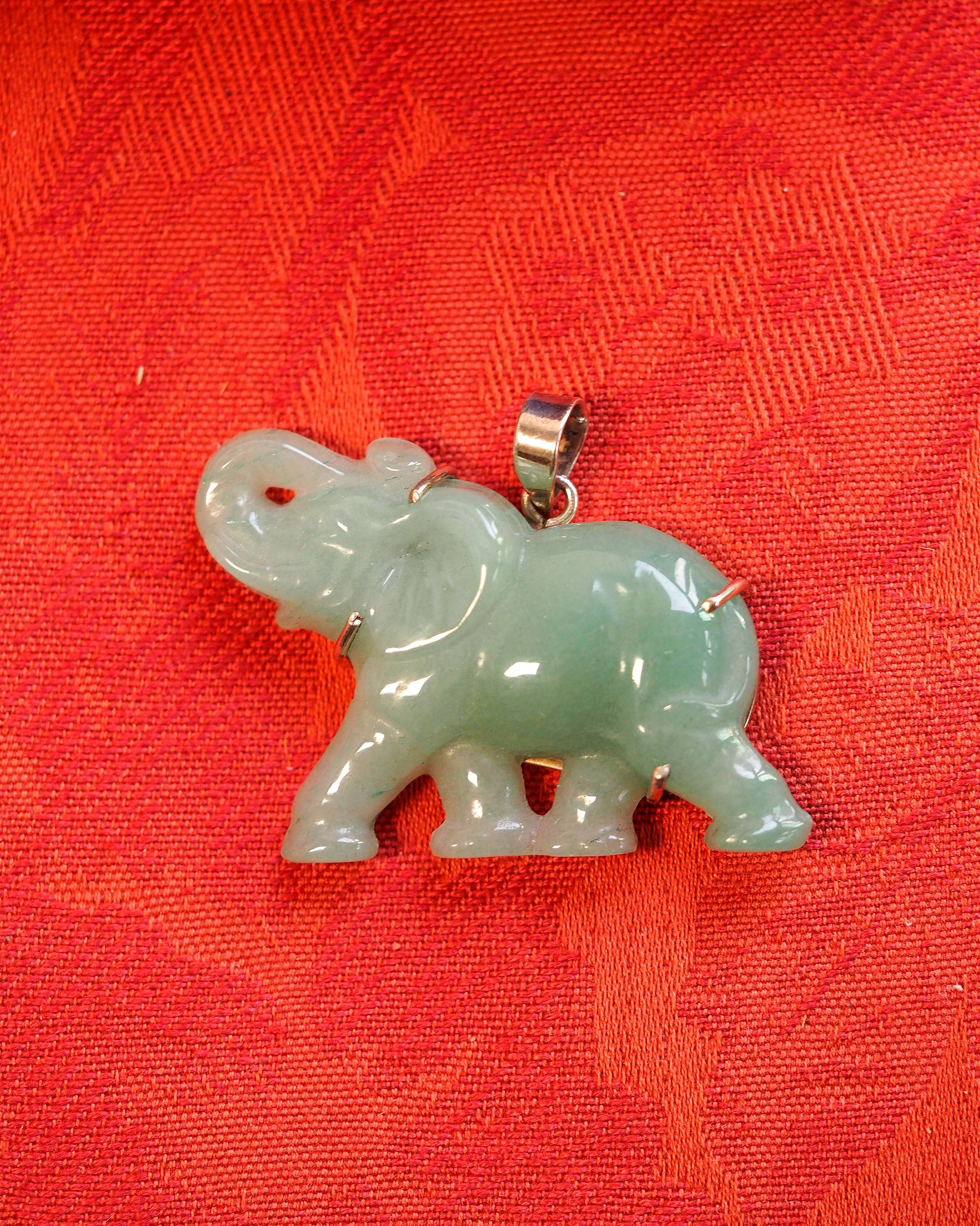 Aventurine elephant pendant on red fabric, side view showing three-dimensional carved silhouette and sterling silver bail