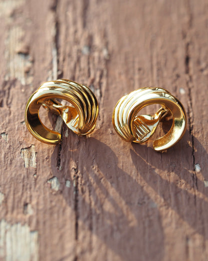 Close-up of Monet gold-plated clip earrings showing the three-tiered swoosh construction and smooth finish