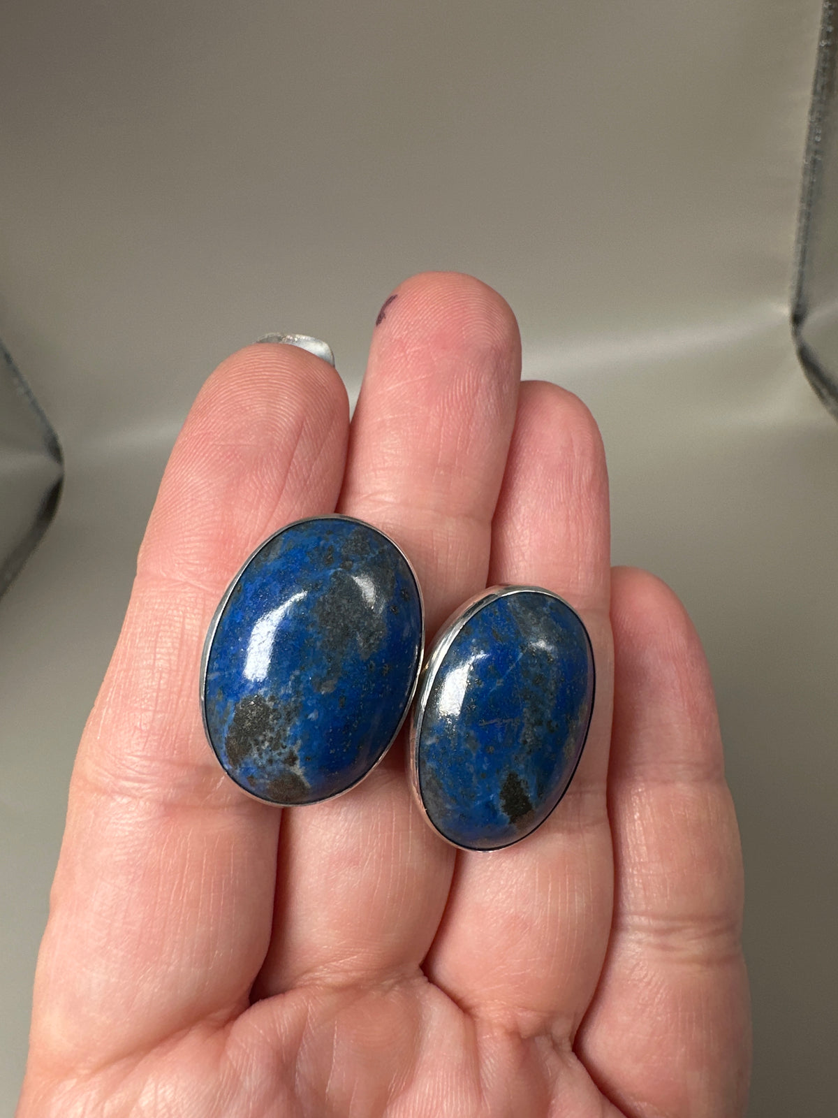 Hand-held scale view of both earrings showing 1-inch size
