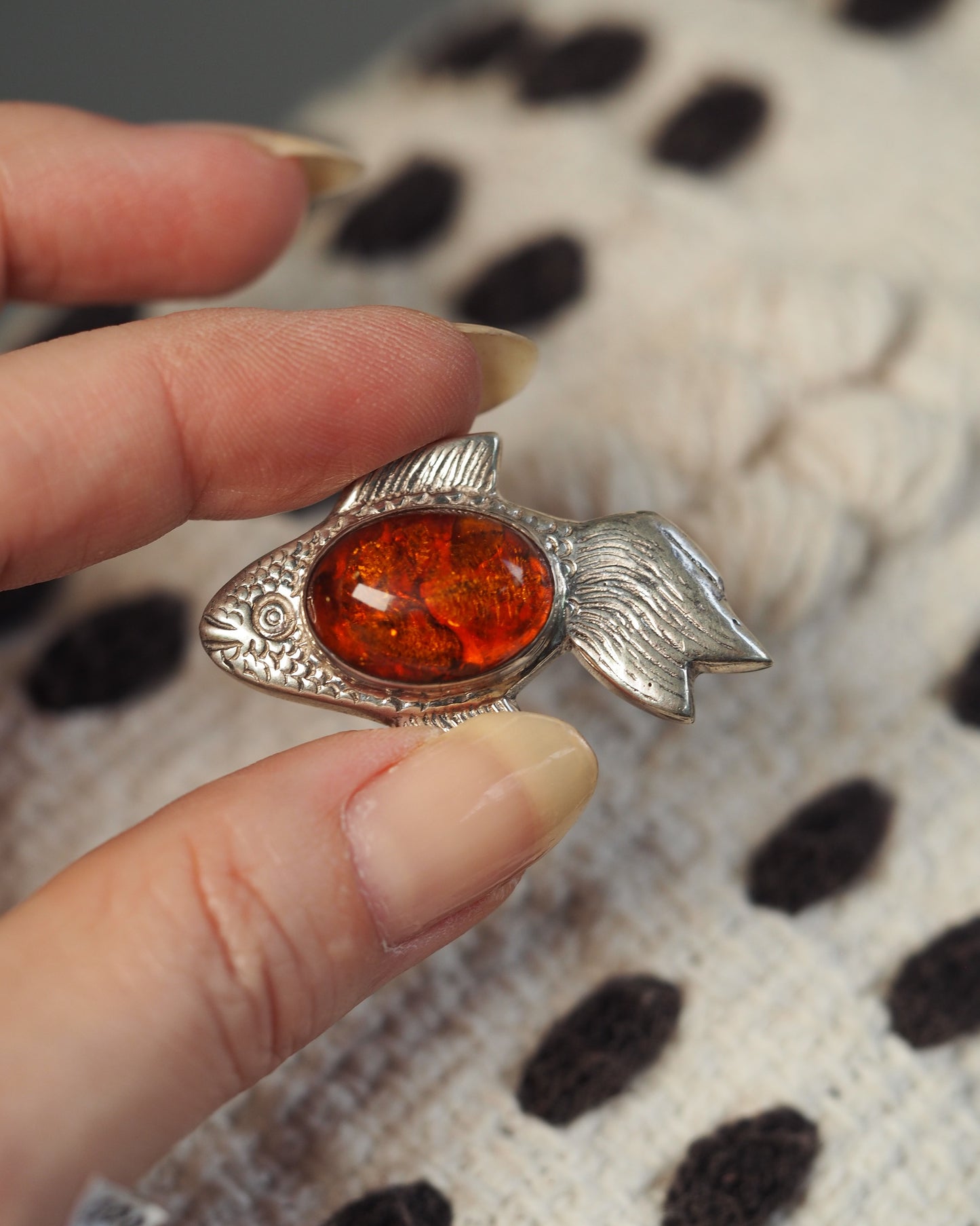 Fish pendant held in fingertips for scale, showing full length and amber translucency