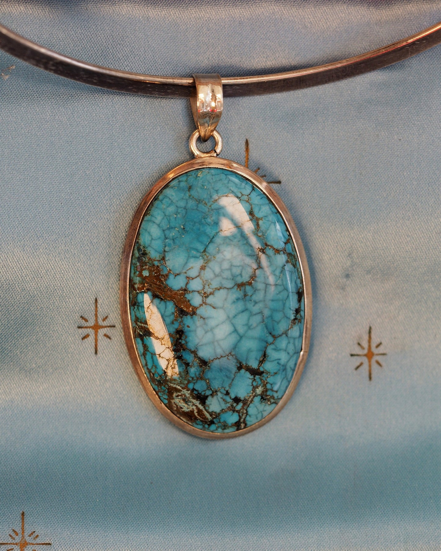 Sterling silver pendant with oval turquoise cabochon, spiderweb matrix in blue and brown, front view on gray background