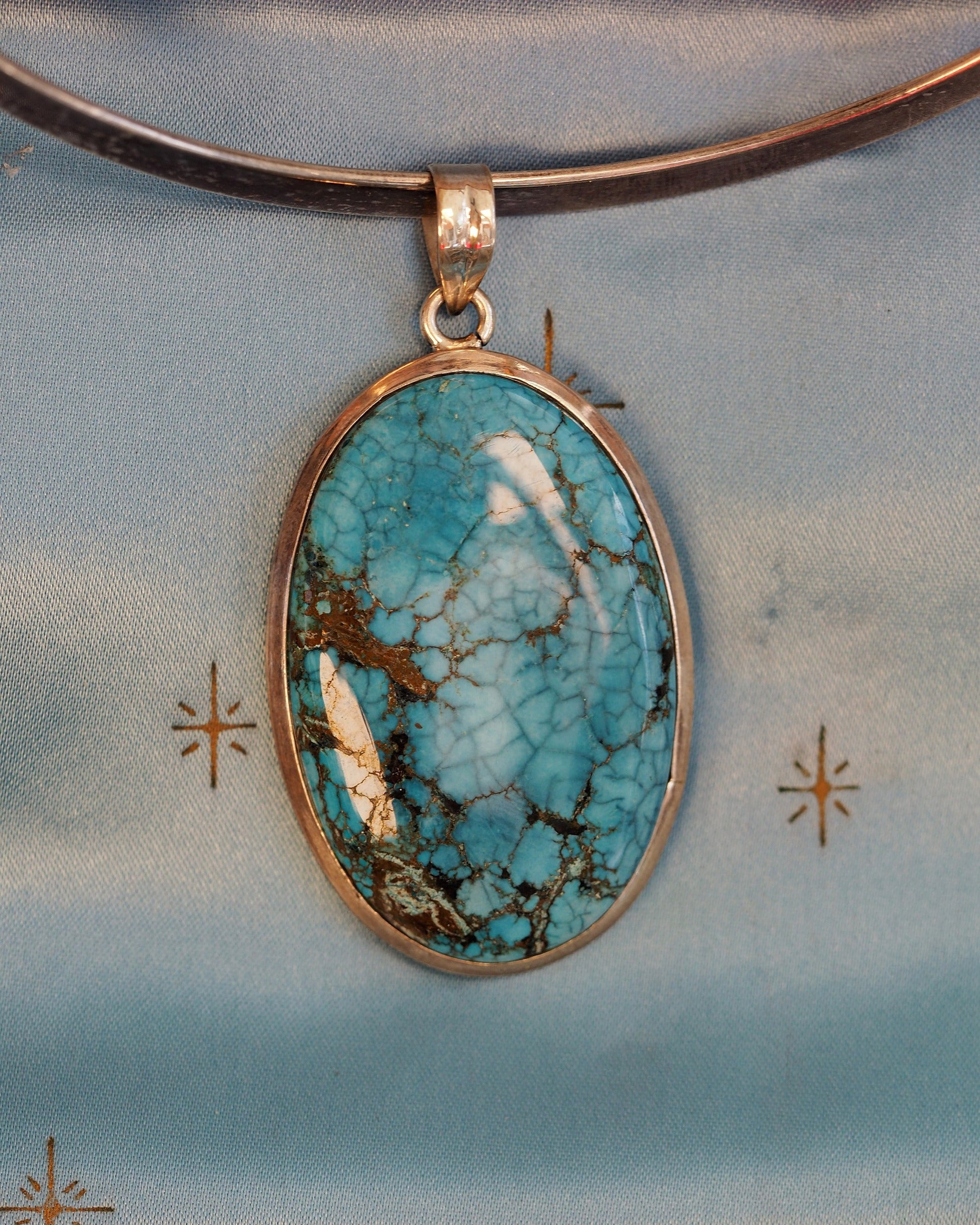 Sterling silver pendant with oval turquoise cabochon, spiderweb matrix in blue and brown, front view on gray background