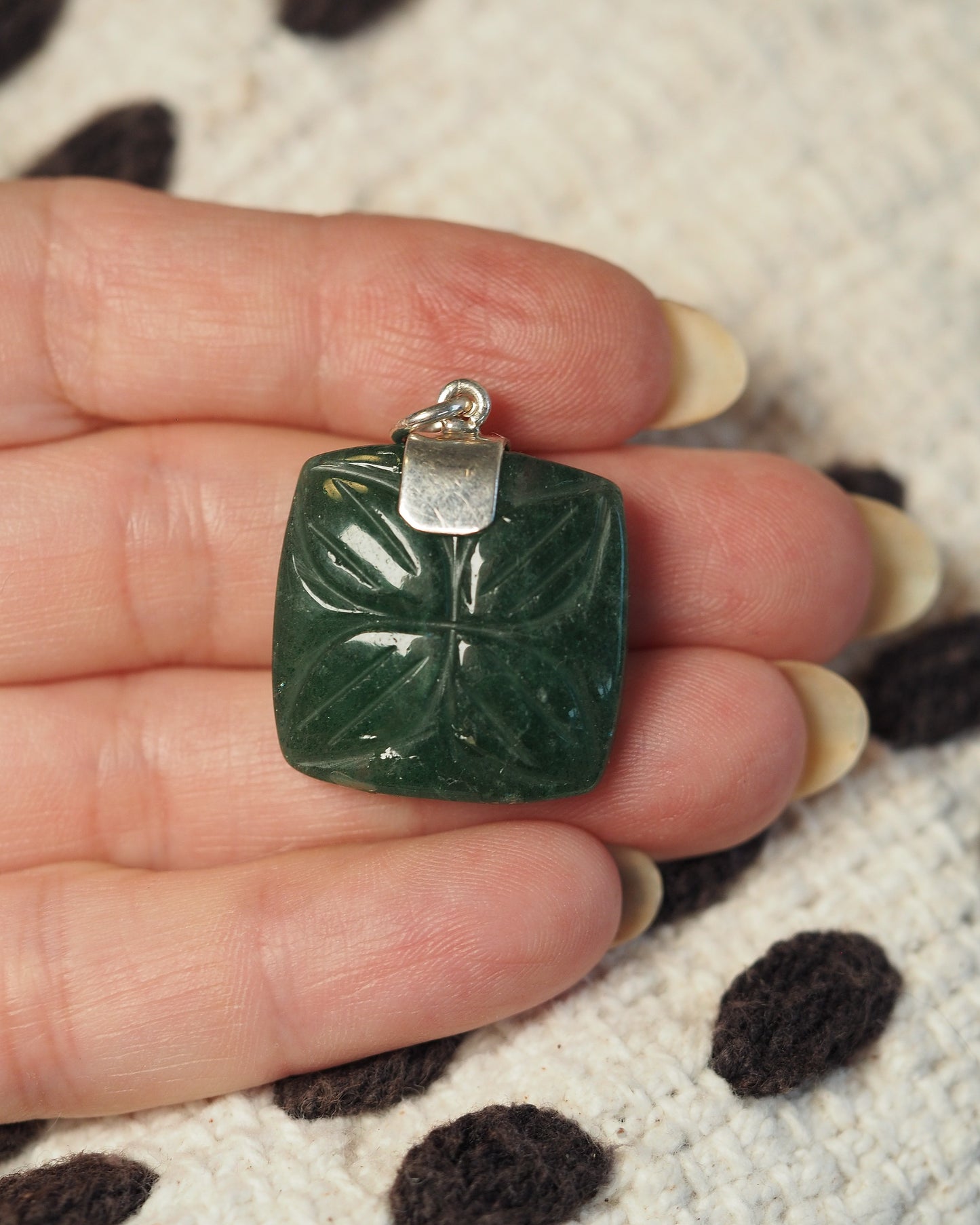 back view of the aventurine pendant on a hand, showing the silver bail and reverse of the carved pattern