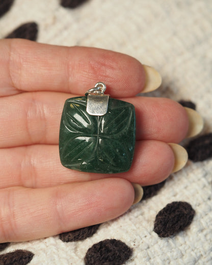back view of the aventurine pendant on a hand, showing the silver bail and reverse of the carved pattern