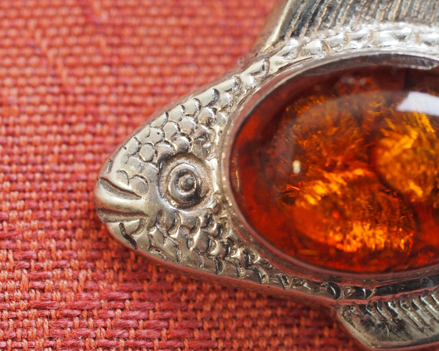 Close-up of fish head showing scale texture, bezel-set amber, and fin detail