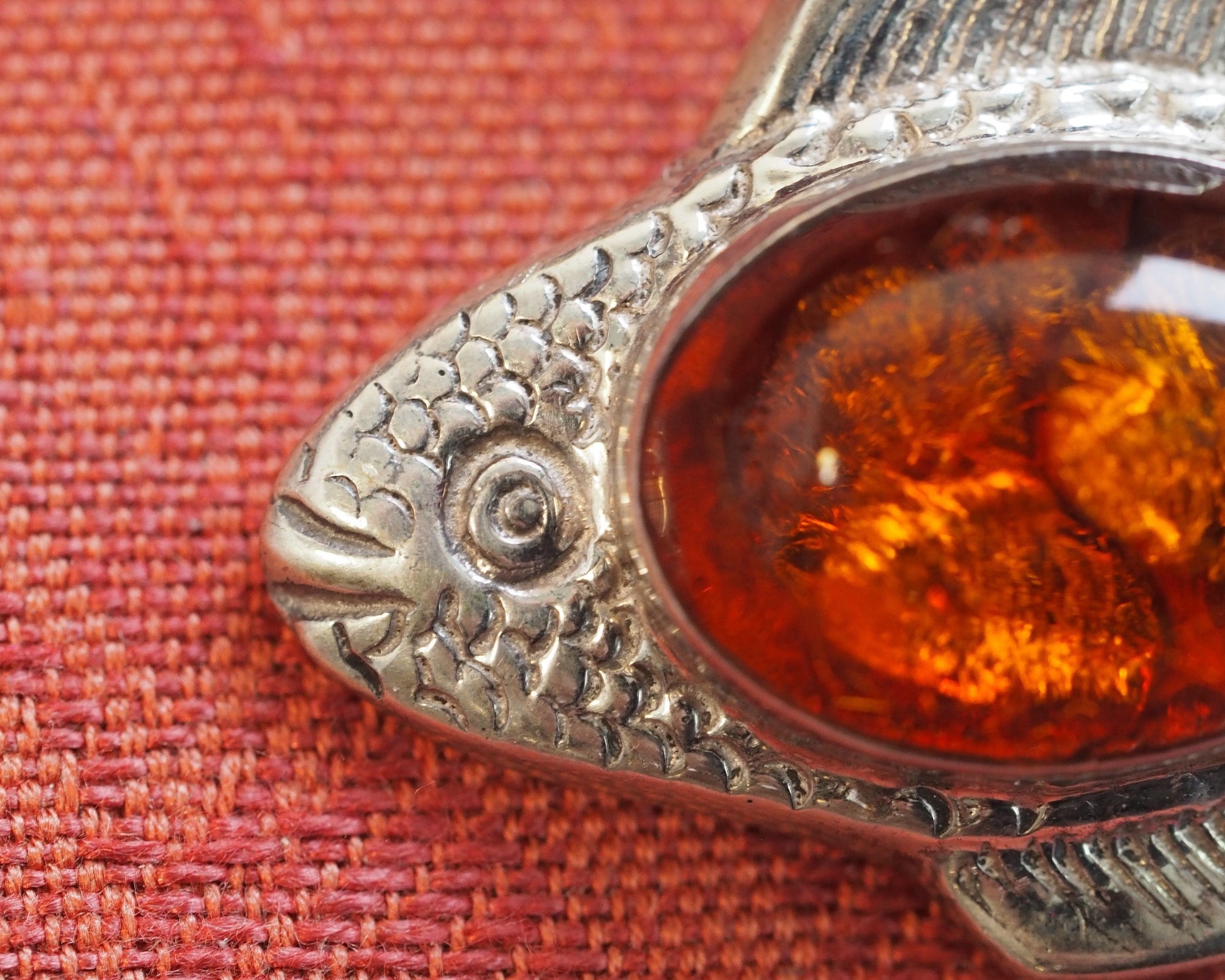 Close-up of fish head showing scale texture, bezel-set amber, and fin detail