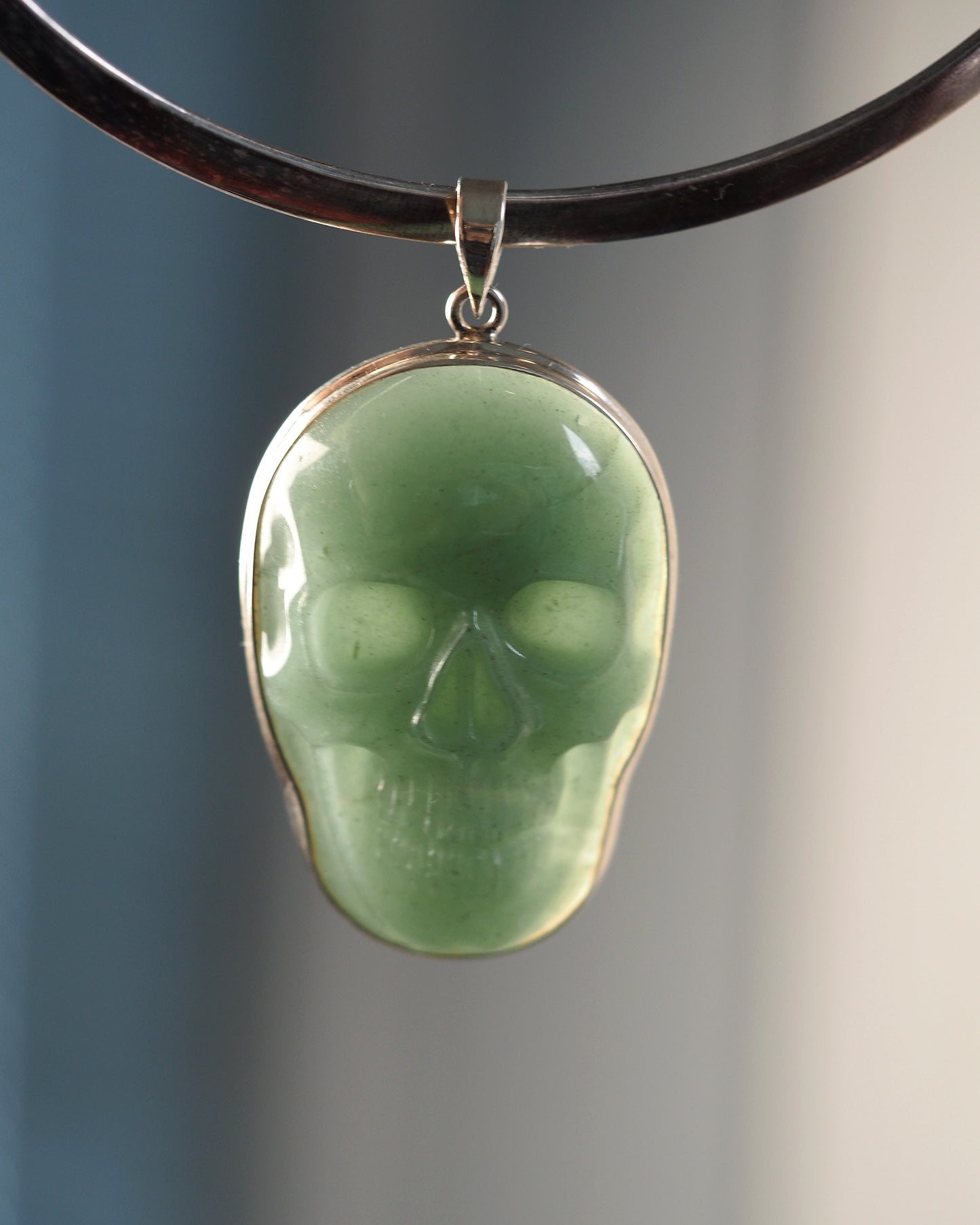 Sterling silver aventurine skull pendant front view, pale green carved stone with eye sockets and teeth detail, shown on black cord