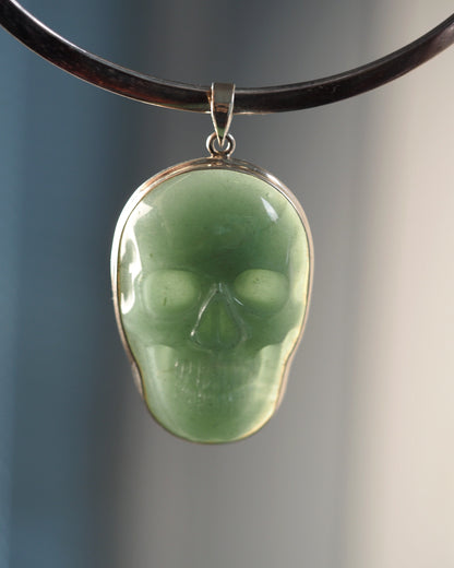 Sterling silver aventurine skull pendant front view, pale green carved stone with eye sockets and teeth detail, shown on black cord