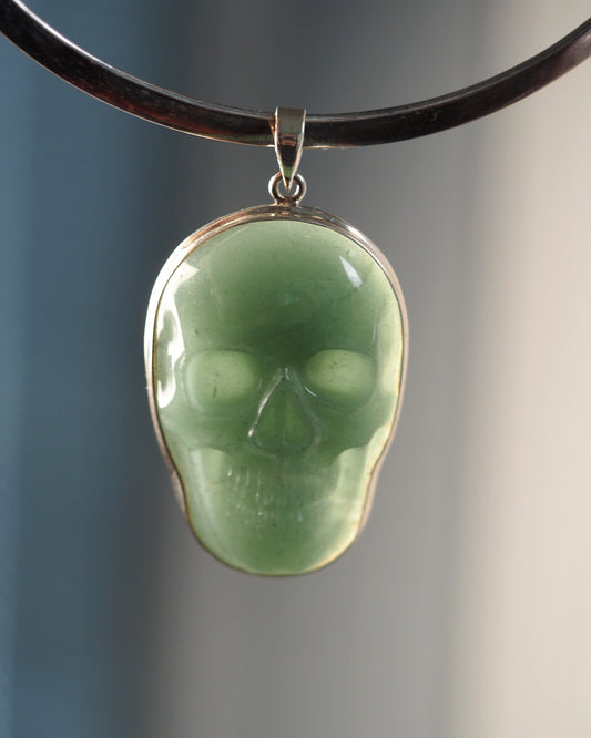 Sterling silver aventurine skull pendant front view, pale green carved stone with eye sockets and teeth detail, shown on black cord