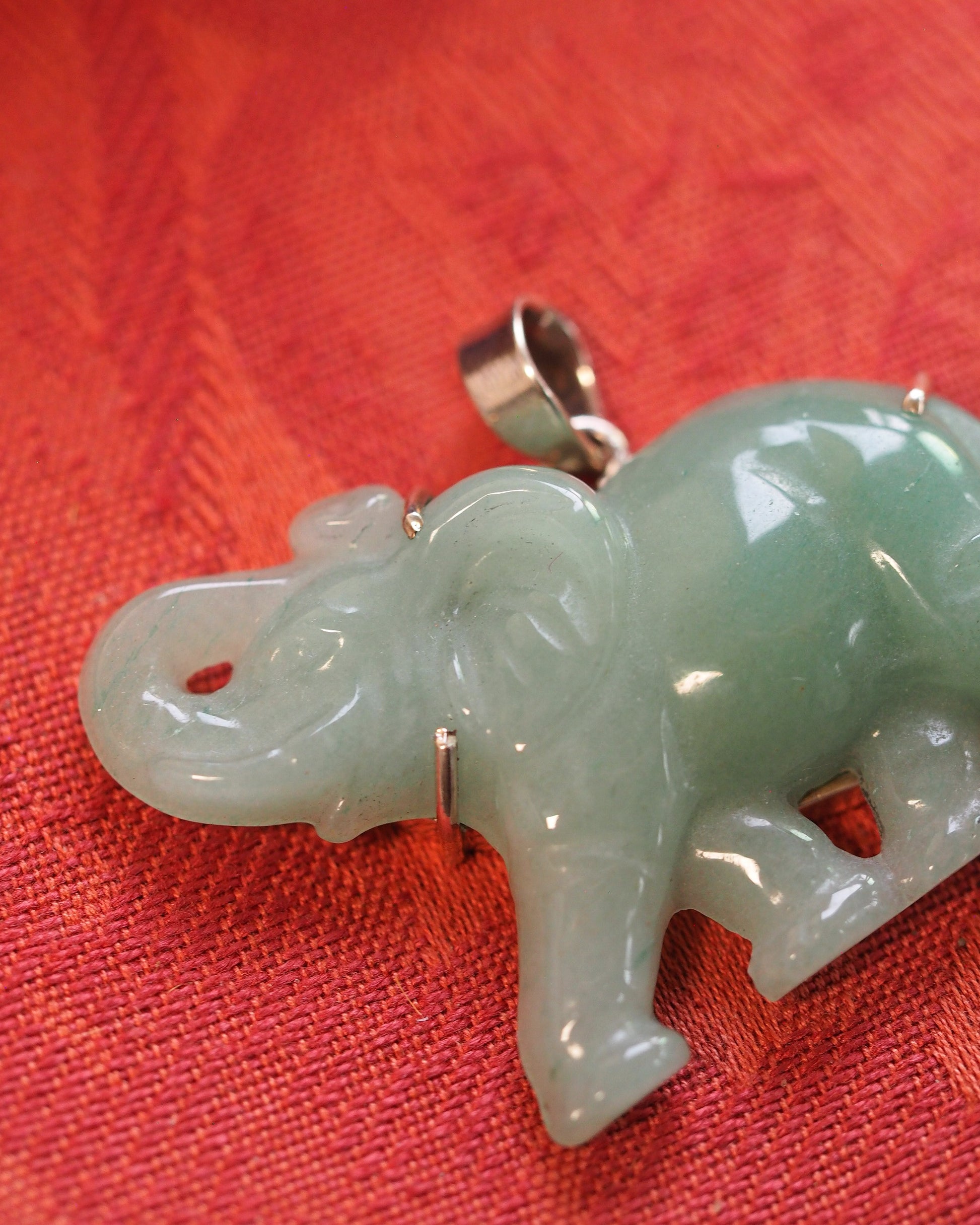 Detail view of carved aventurine elephant head and trunk on red fabric, showing stone's natural cloudy inclusions