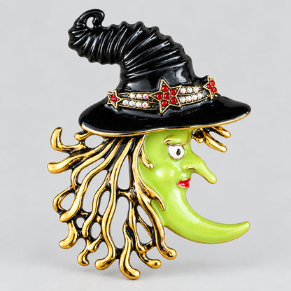 Vintage Kirks Folly witch brooch with green enamel face, black hat, rhinestones and gold-tone fringe, front view