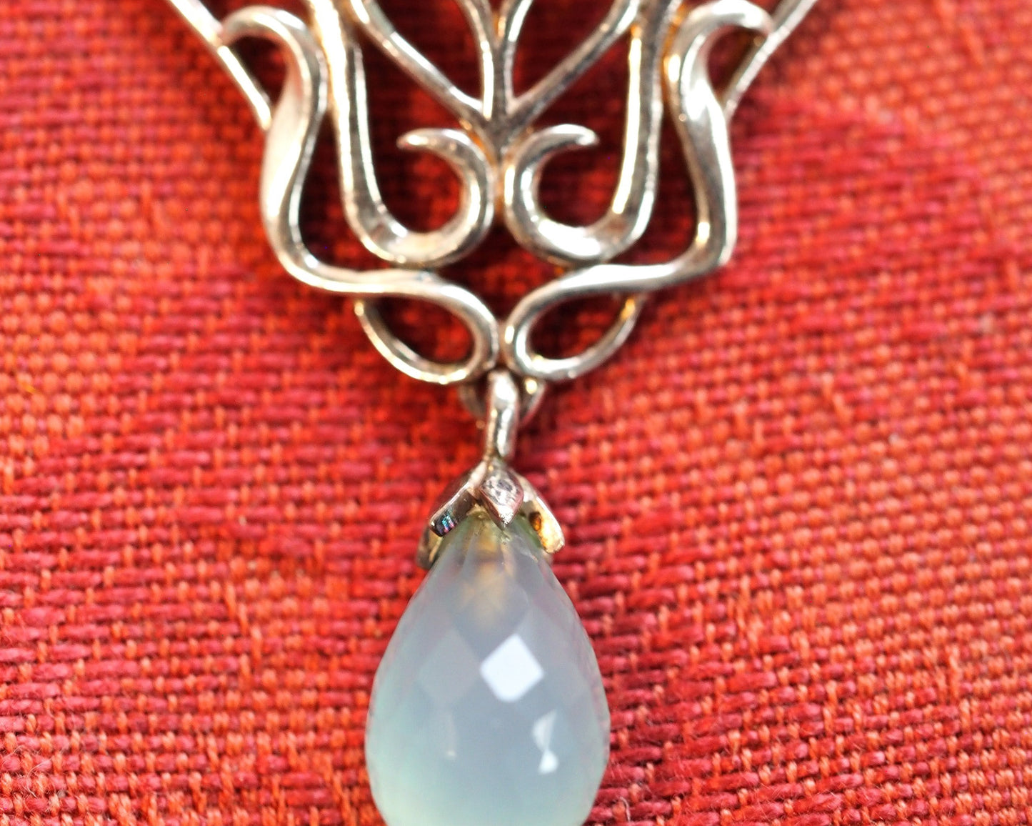 Close-up of faceted chalcedony teardrop dangle and lower scrollwork detail on Derewala pendant