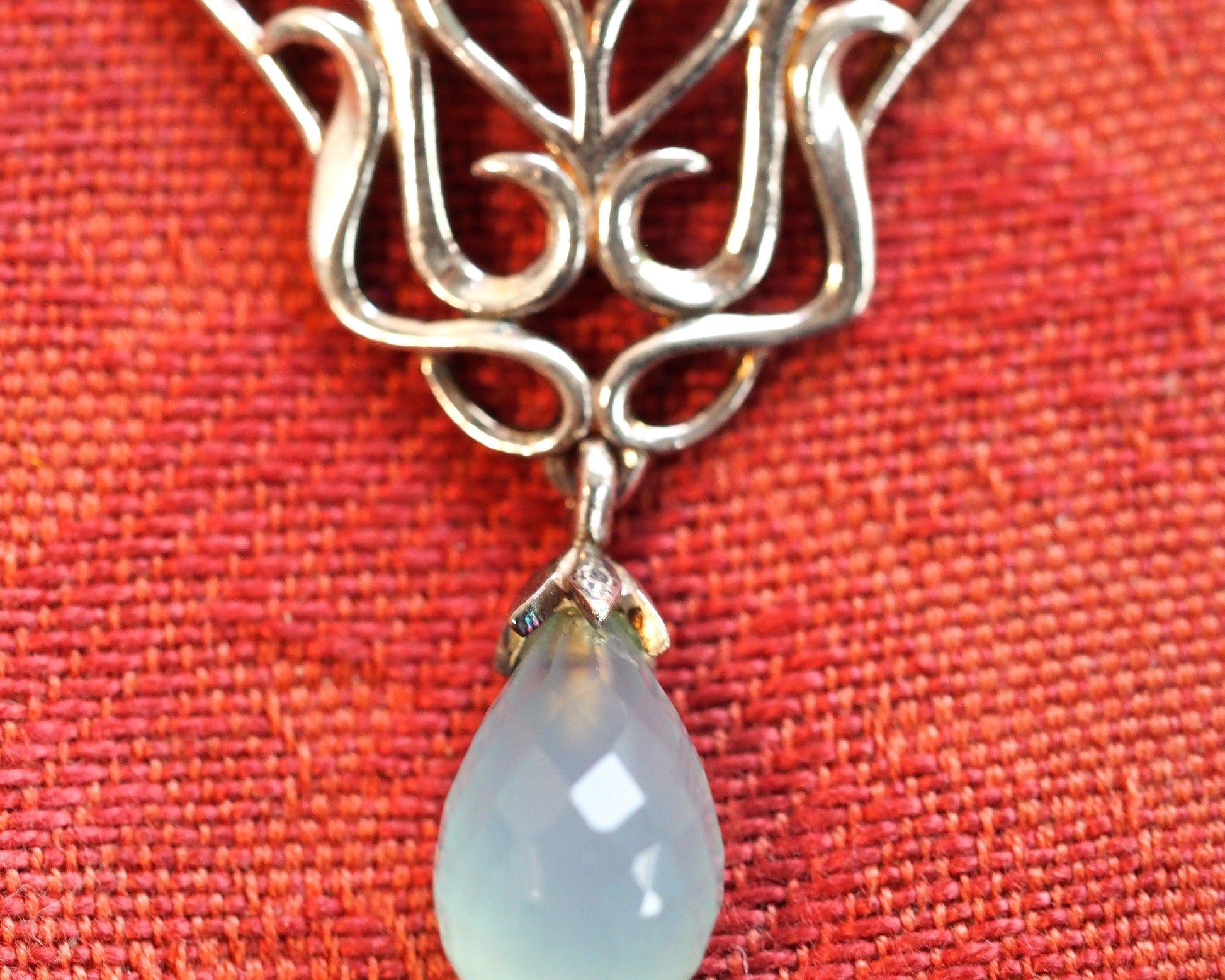 Close-up of faceted chalcedony teardrop dangle and lower scrollwork detail on Derewala pendant