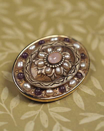 Close-up of Michal Golan brooch with rose-colored quartz cabochon, pearl-like petals, and engraved scrollwork