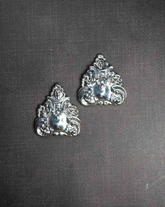 Sterling silver repousse clip earrings with triangular silhouette and scroll motif, front view on gray background
