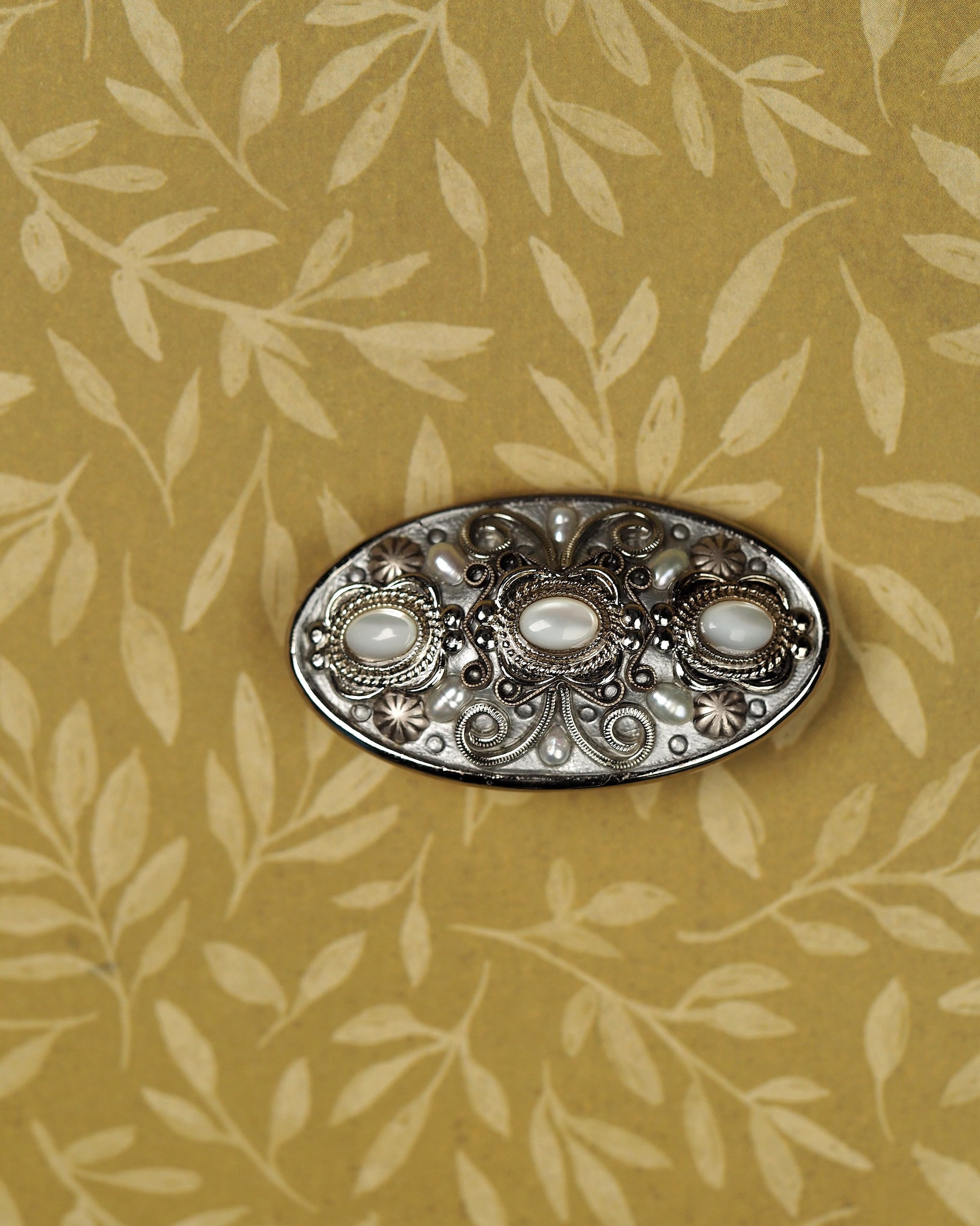 Signed Michal Golan silver-tone filigree brooch with three pale cat's-eye cabochons, front view