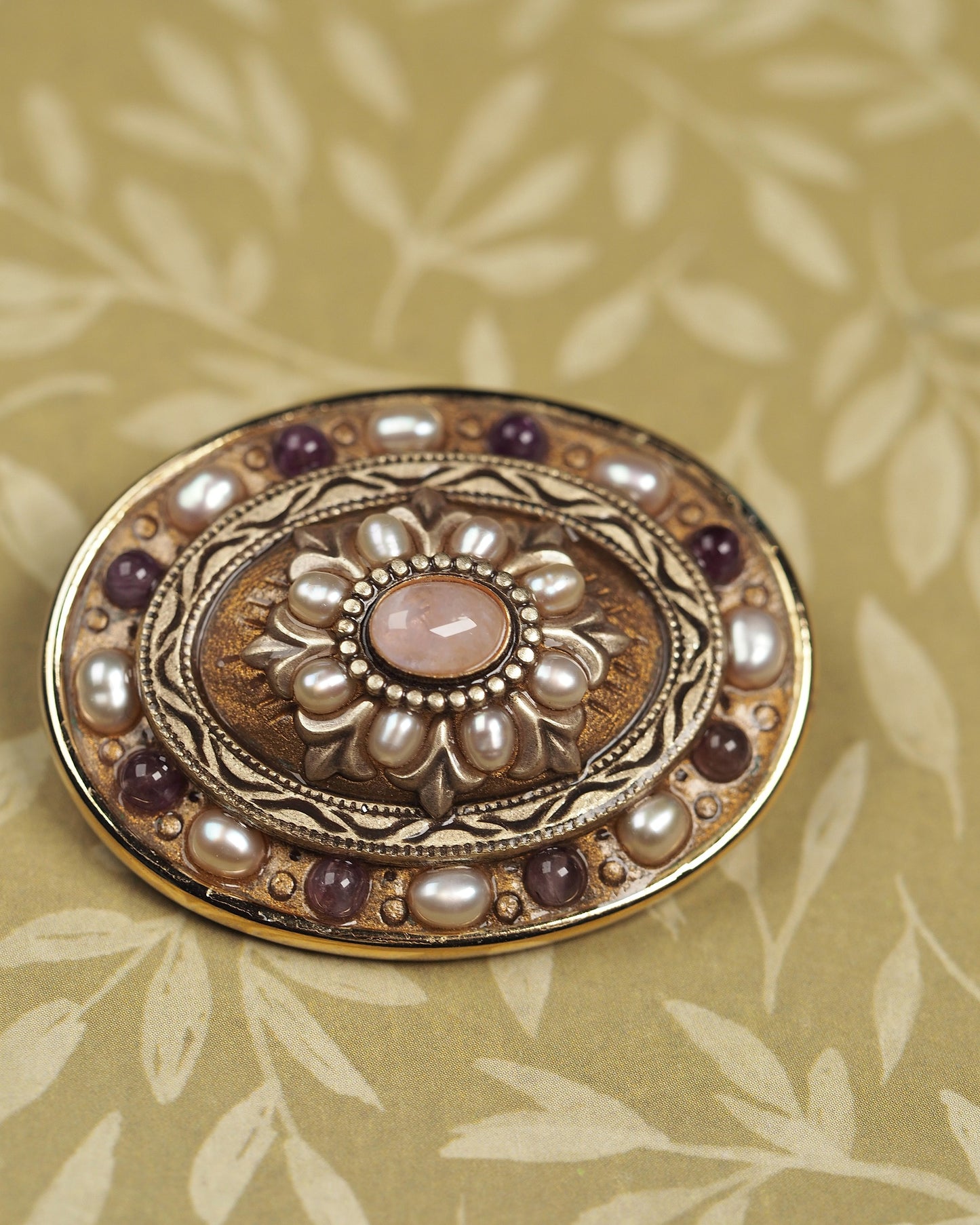 Detail of concentric rings with pearl-like beads, engraved leaves, and purple cabochons on Michal Golan brooch
