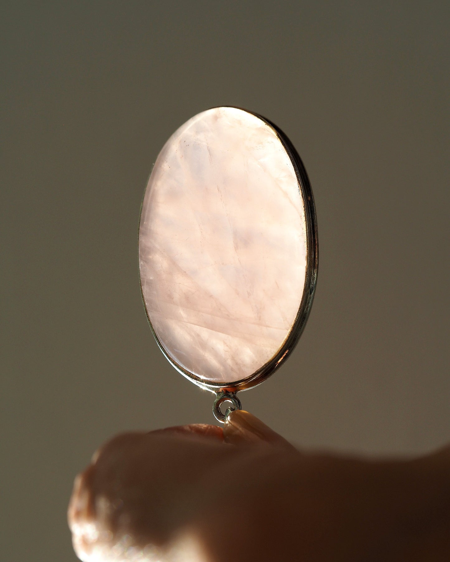 Rose quartz pendant held upright on fingertip, backlit to show translucency and internal facets