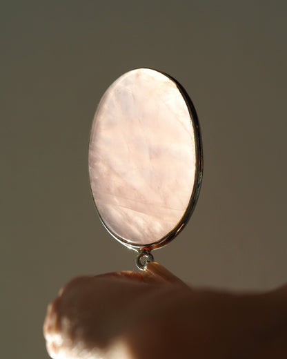 Rose quartz pendant held upright on fingertip, backlit to show translucency and internal facets