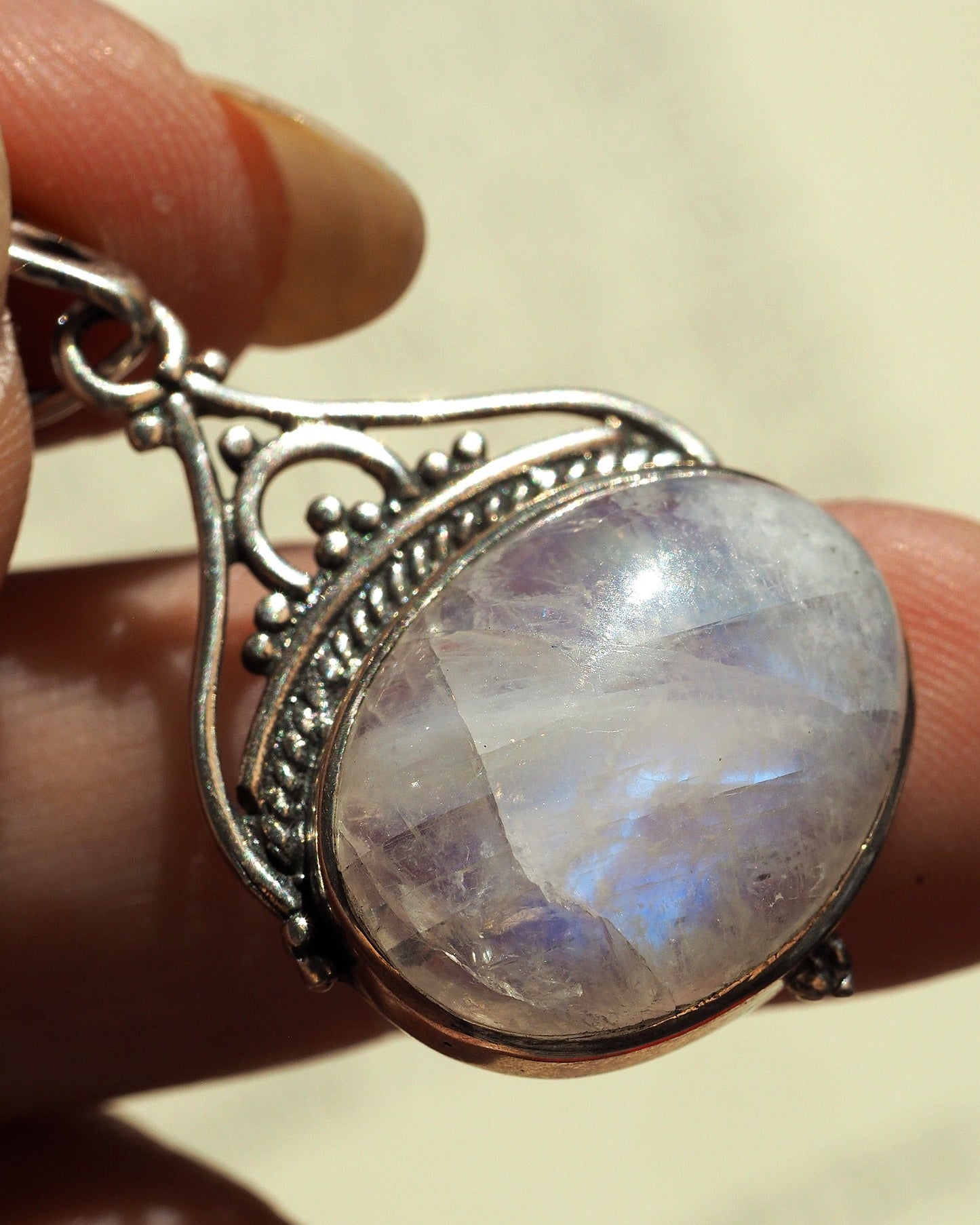Rainbow moonstone pendant held on fingertips for scale, showing faceted stone dome and articulated bail