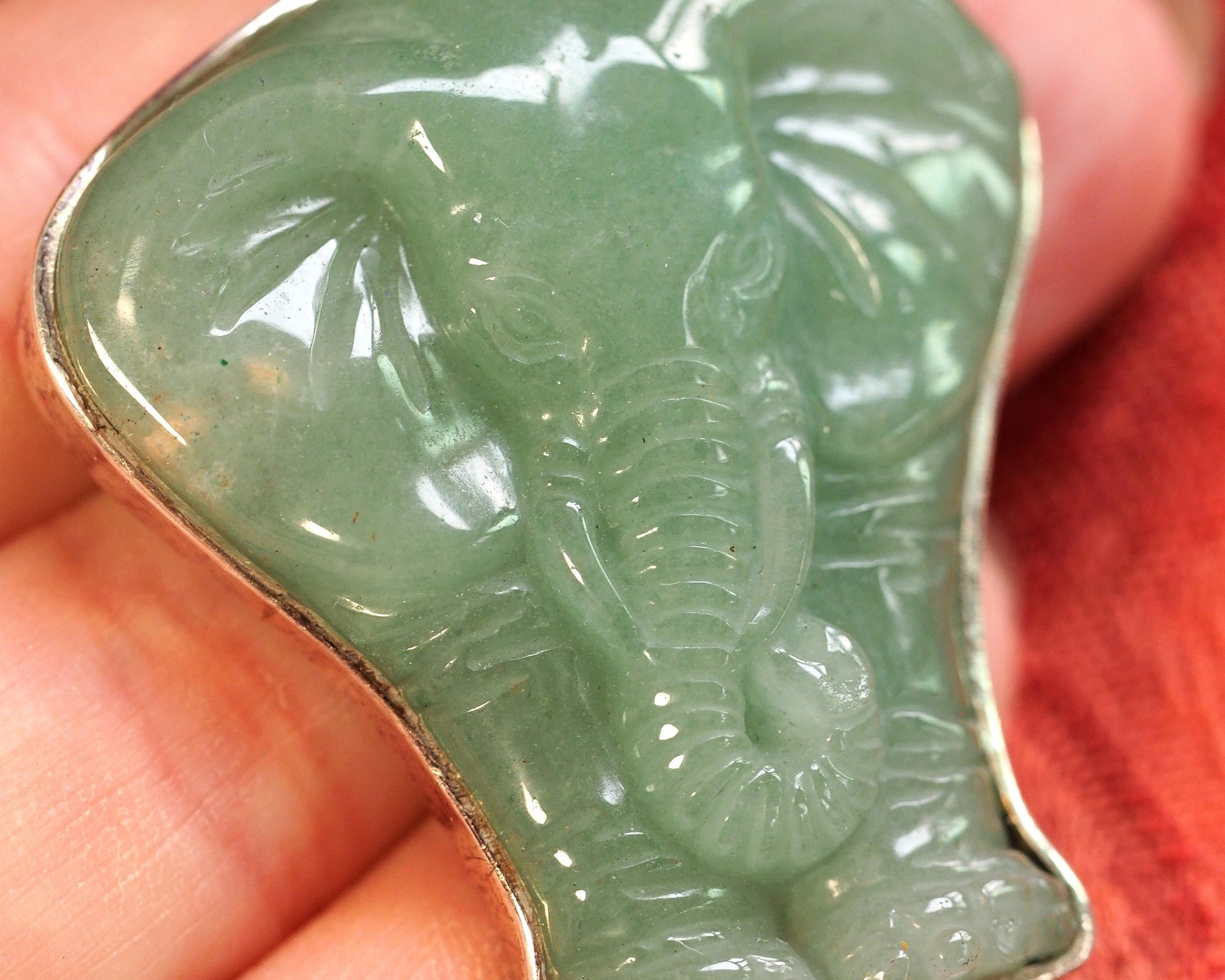 Aventurine elephant pendant held on fingertip for scale, showing two-inch height and dimensional carved relief