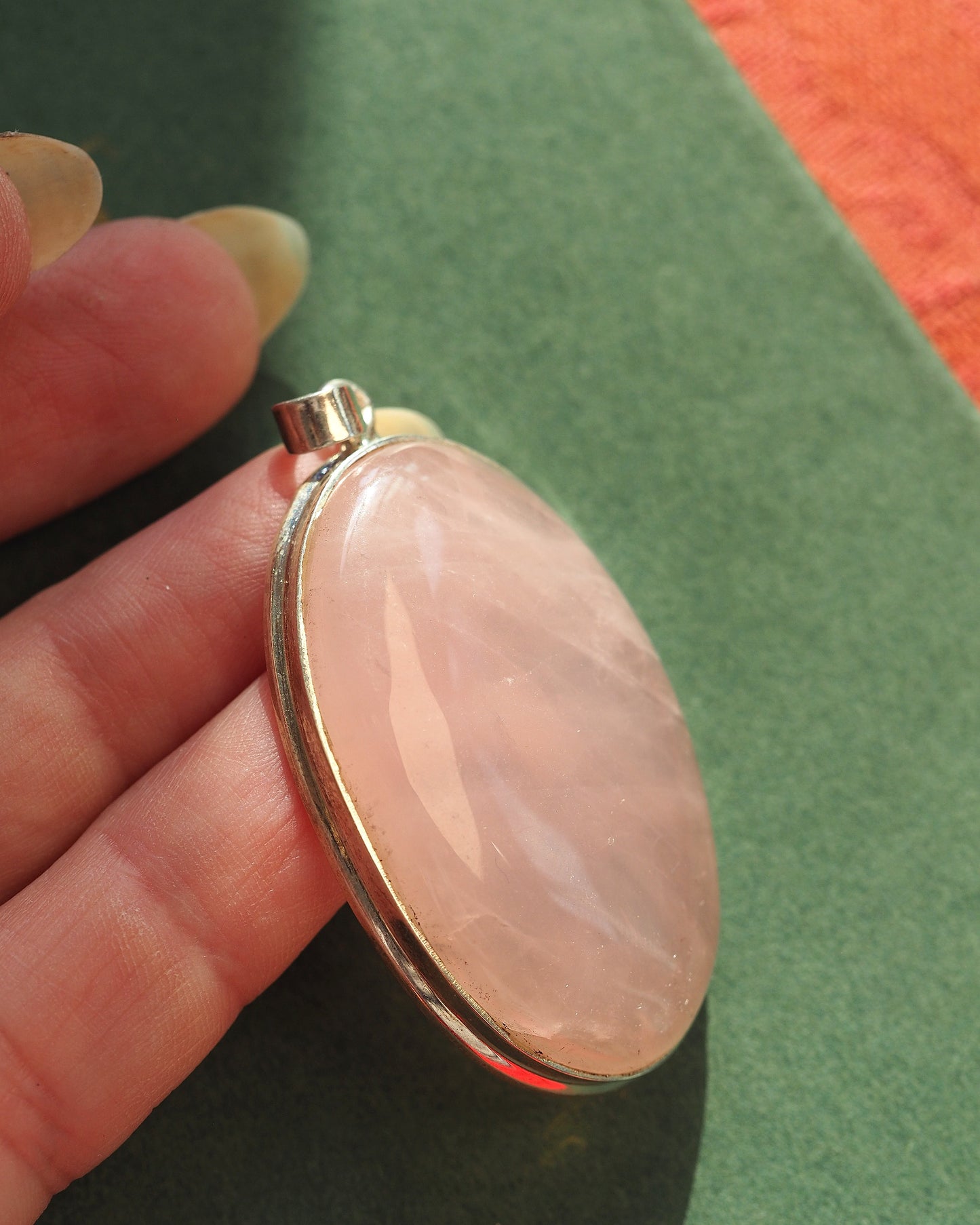 Rose quartz pendant shown on fingertip for scale, 1 inch oval stone in sterling bezel setting